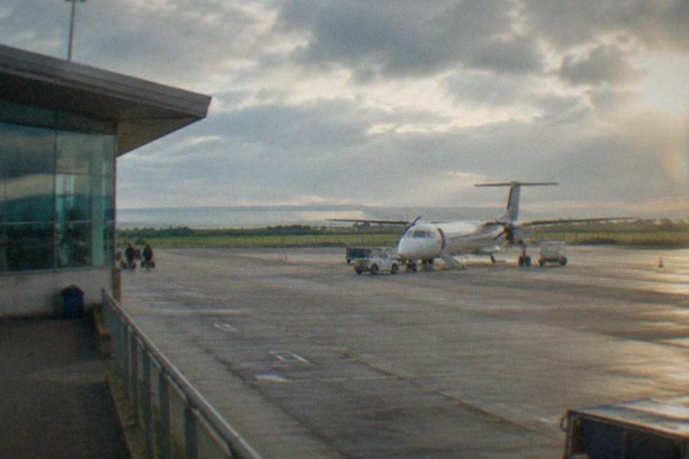 A regional airport terminal building under a bright sky with a parked aircraft on the apron