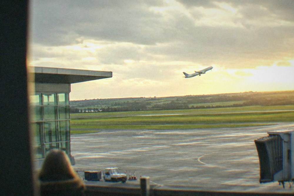 A passenger aircraft climbing away from a runway with green fields beyond the airfield boundary