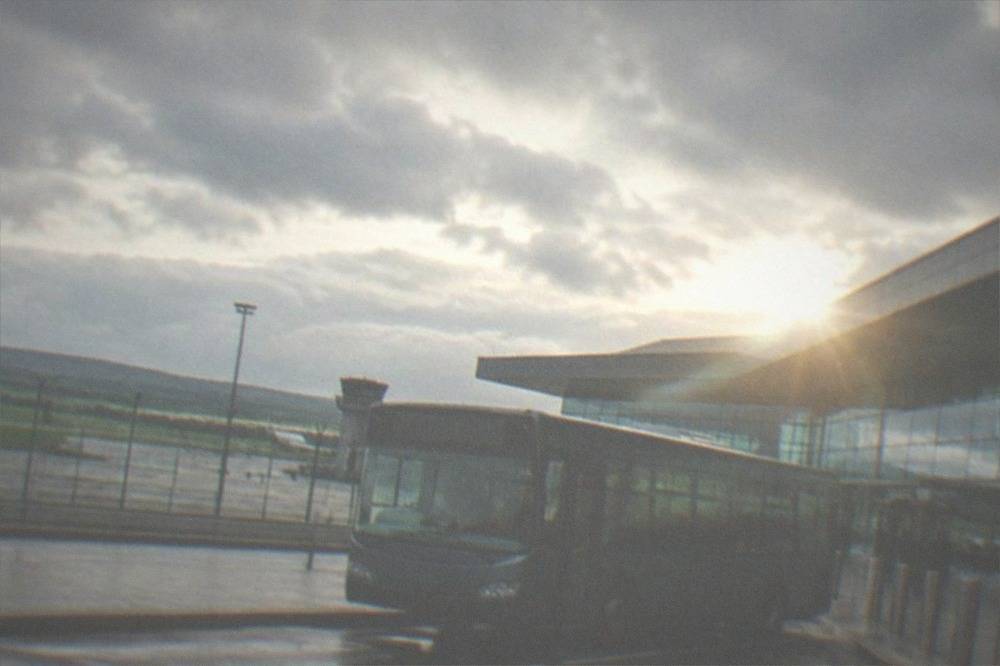 A single-decker bus parked at an airport kerbside with the terminal behind it
