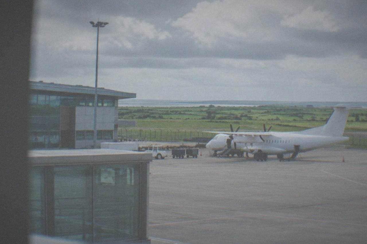 A regional airport terminal building under a bright sky with a parked aircraft on the apron