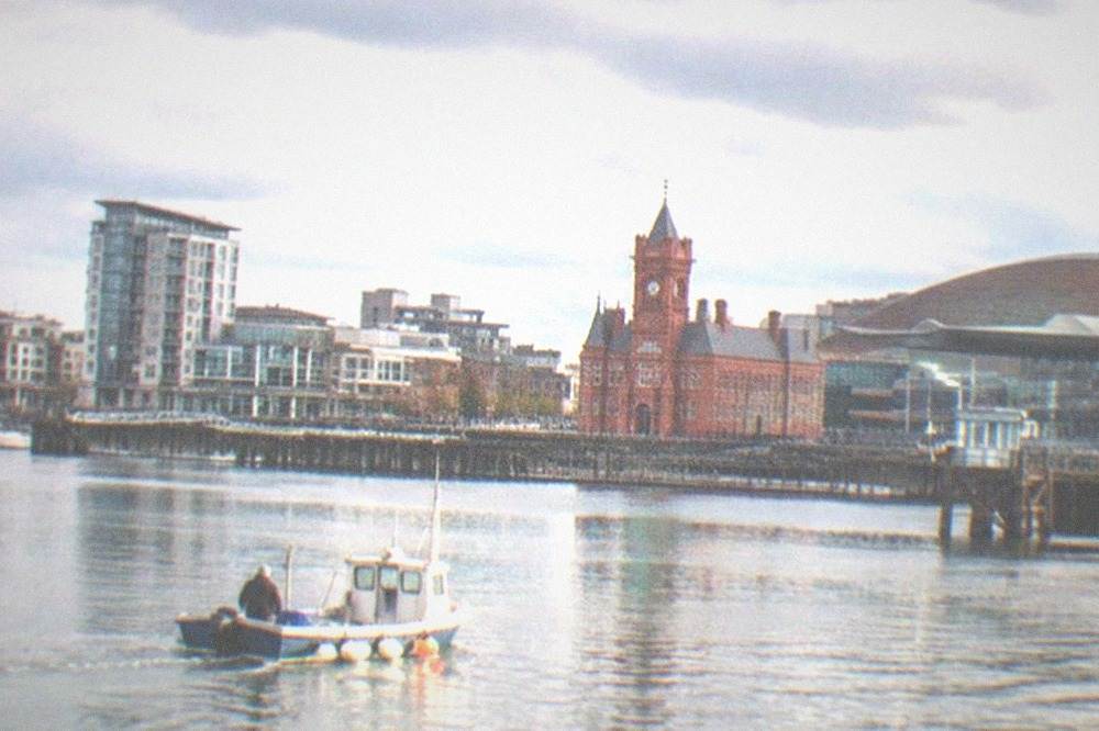 Small boat on Cardiff Bay with waterfront buildings behind