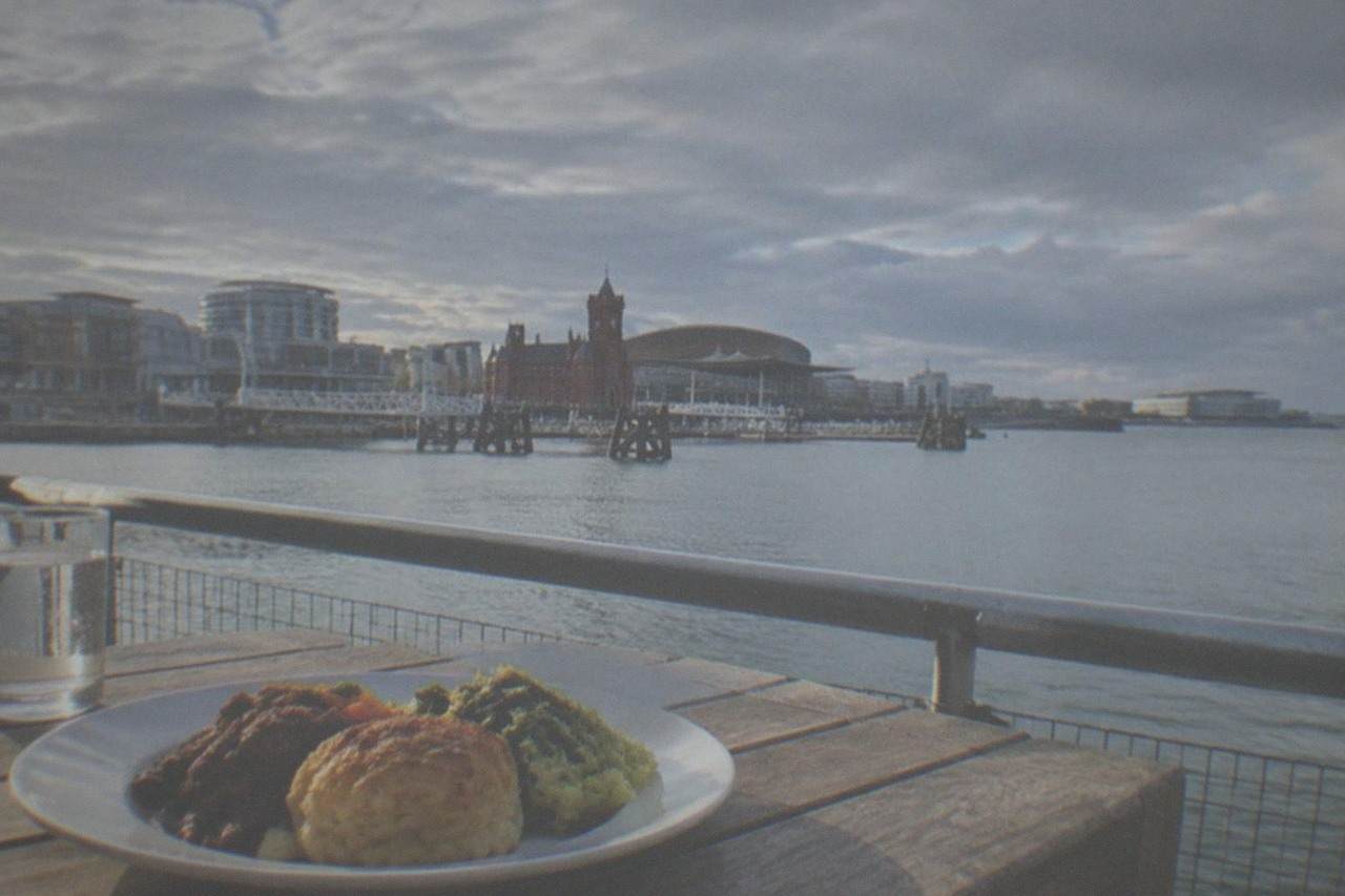 A plate of Welsh food on a table overlooking Cardiff Bay