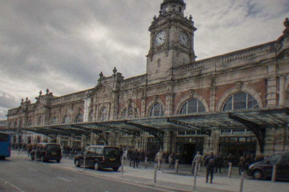 Station facade with clock tower above a busy entrance forecourt