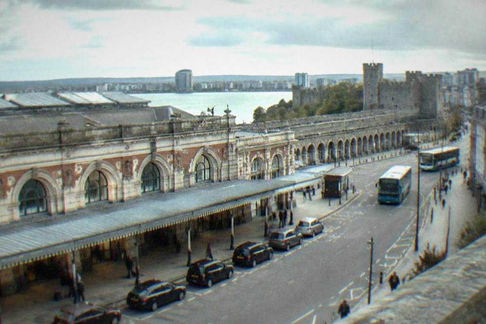 City street with Victorian arcades and a stone castle wall beyond