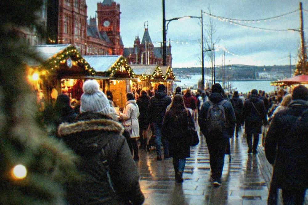 Crowded pedestrian shopping street with market stalls and Christmas lights at dusk