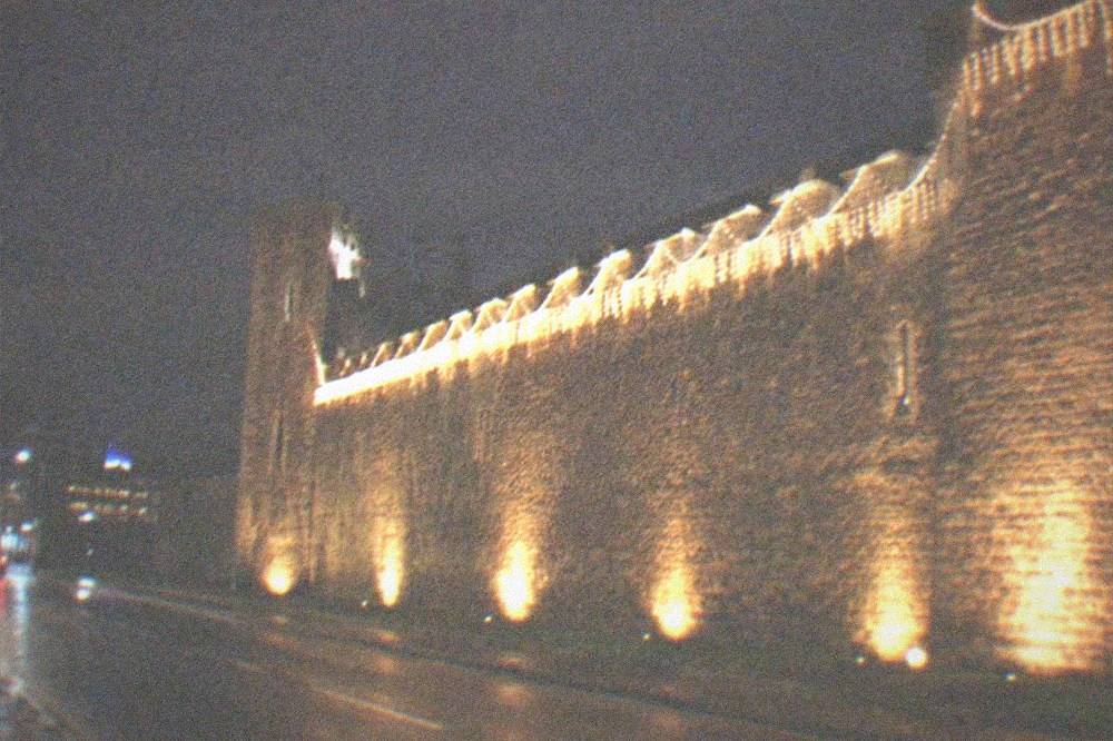 Historic castle walls lit by festive lights above a city street at night