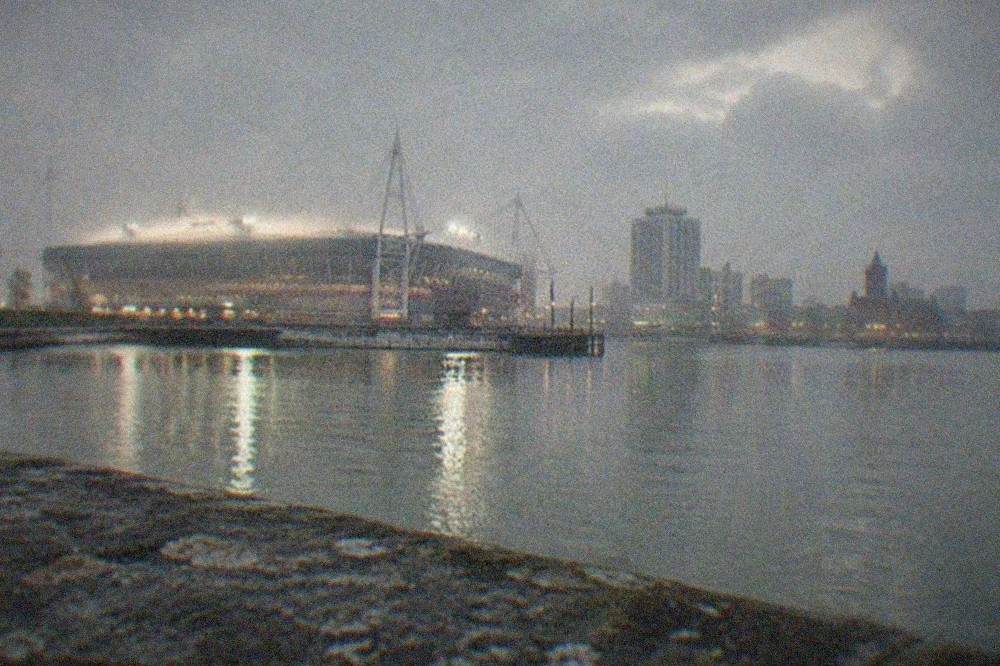 A floodlit stadium towering over a city skyline at dusk