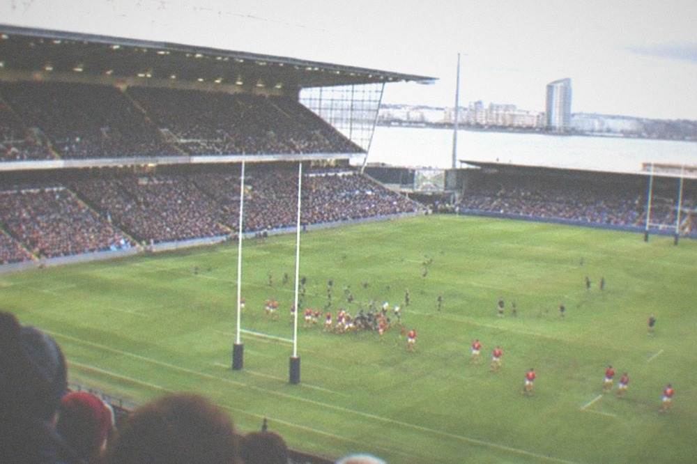 A packed rugby stadium seen from high in the stands during a daytime match