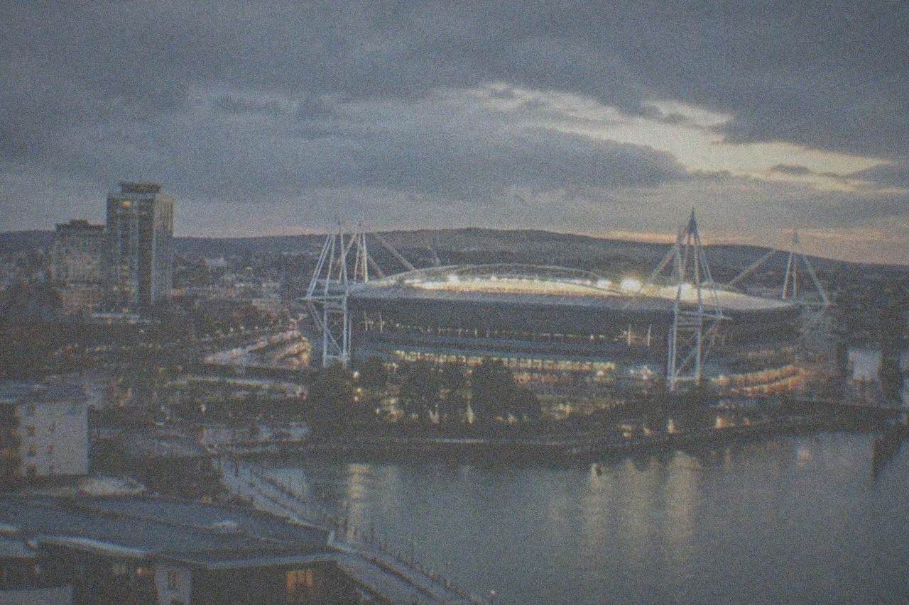 A floodlit stadium towering over a city skyline at dusk