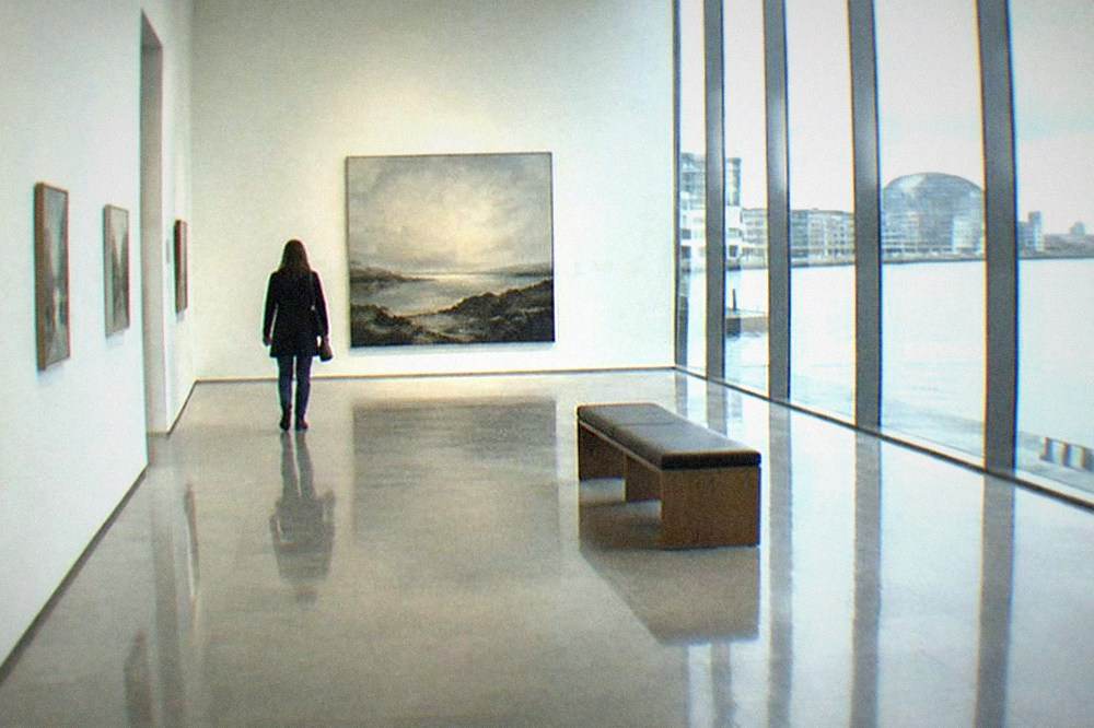 A bright gallery hall with paintings hung along the walls and polished stone floors