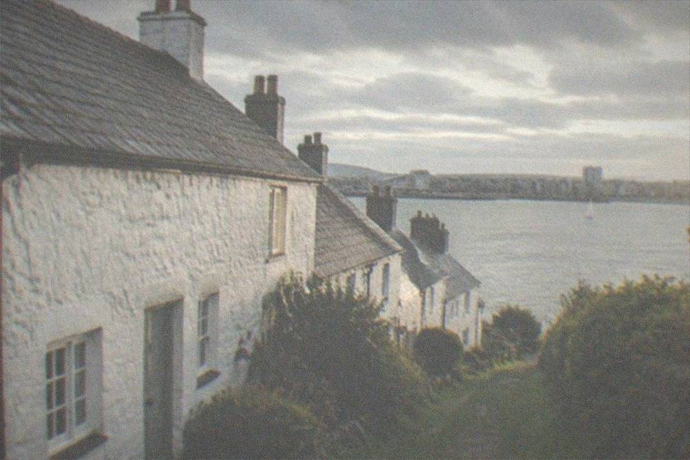 A row of white-washed historic stone cottages with slate roofs beside a grassy lane