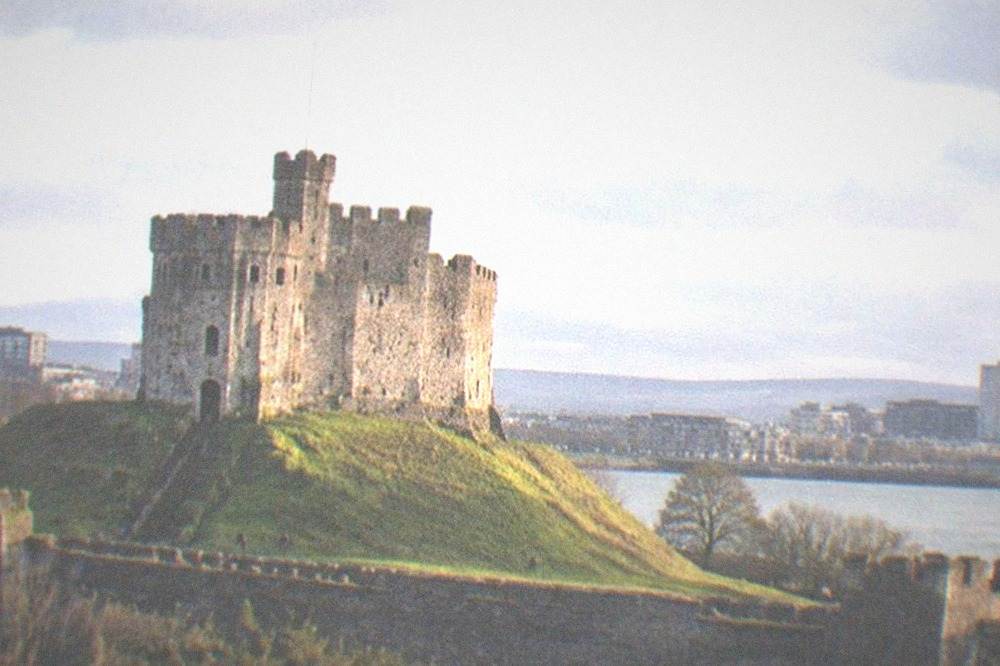 A stone keep on a grassy mound above old castle walls in the late afternoon