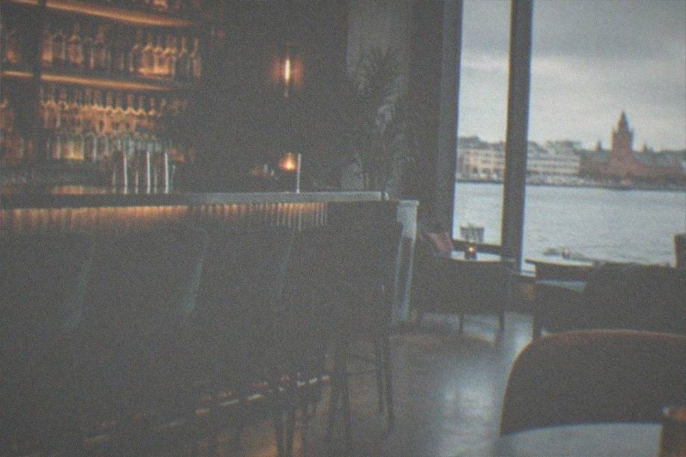 Dimly lit cocktail bar interior with backlit bottle shelves and bar stools