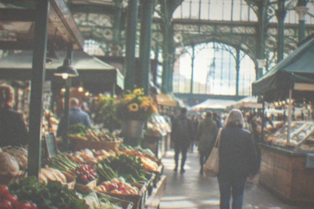 Interior of a Victorian market hall with food stalls and shoppers under an iron and glass roof