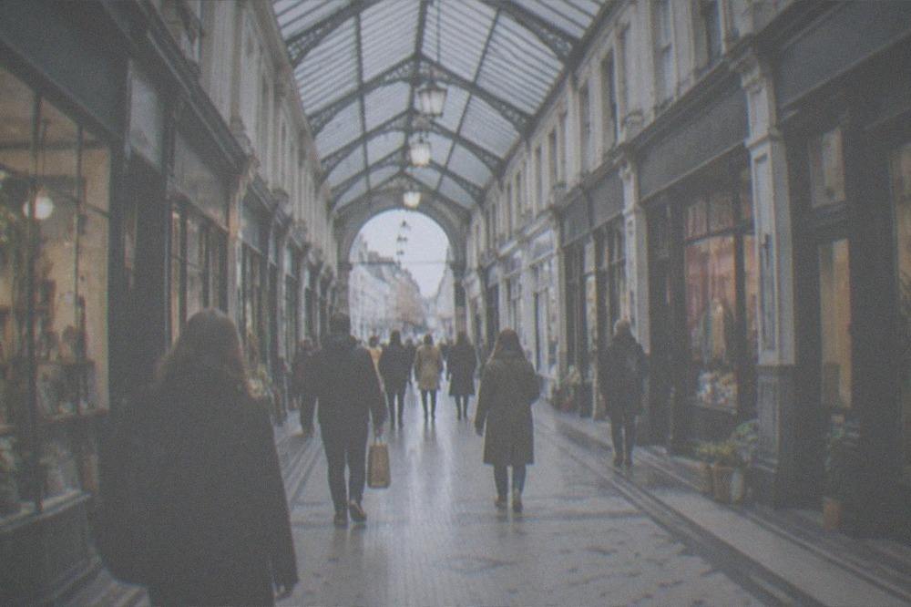 Shoppers walking through a covered Victorian shopping arcade with small independent storefronts