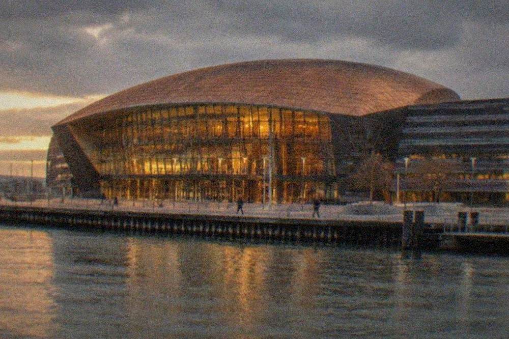 The illuminated facade of the Wales Millennium Centre at dusk with the Cardiff Bay waterfront in the foreground