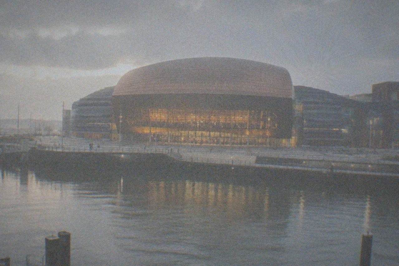 The illuminated facade of the Wales Millennium Centre at dusk with the Cardiff Bay waterfront in the foreground