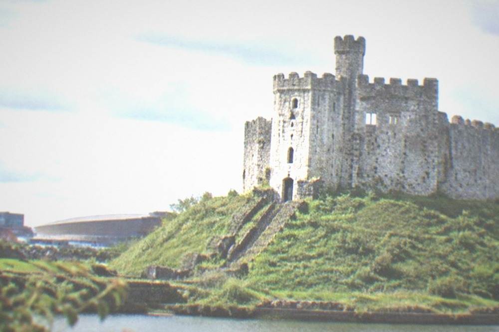 Stone keep of a medieval castle rising above grassy earthworks