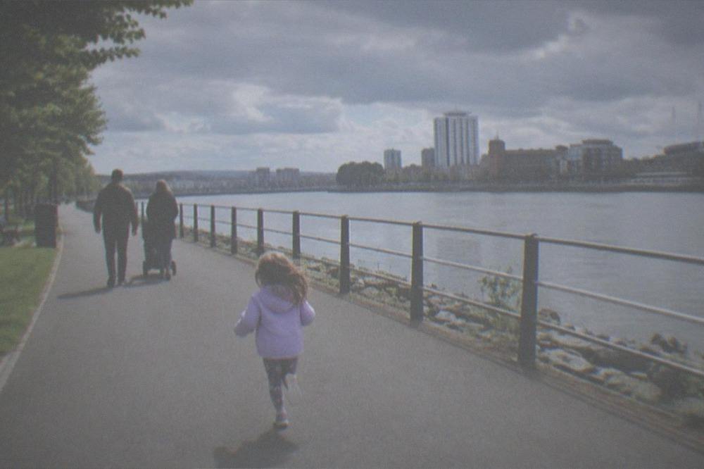 Family walking a wide park path beside a river in late afternoon light