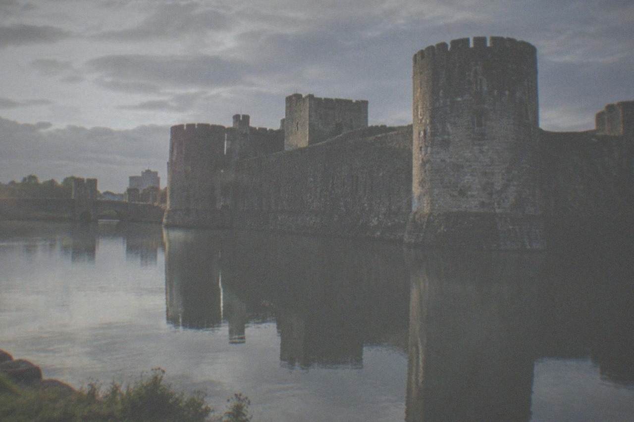 A stone castle with towers reflected in a large water moat under a bright sky