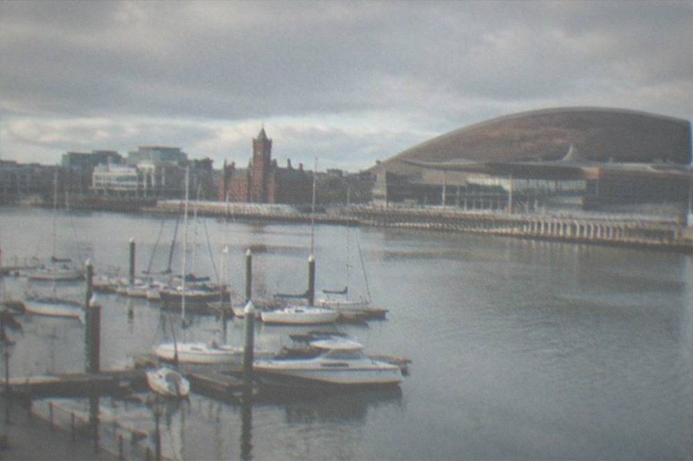 Waterfront buildings and boats along a wide bay with a modern arts centre facade