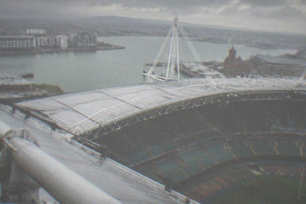 The steeply banked stands of a large stadium seen from high on the roof structure