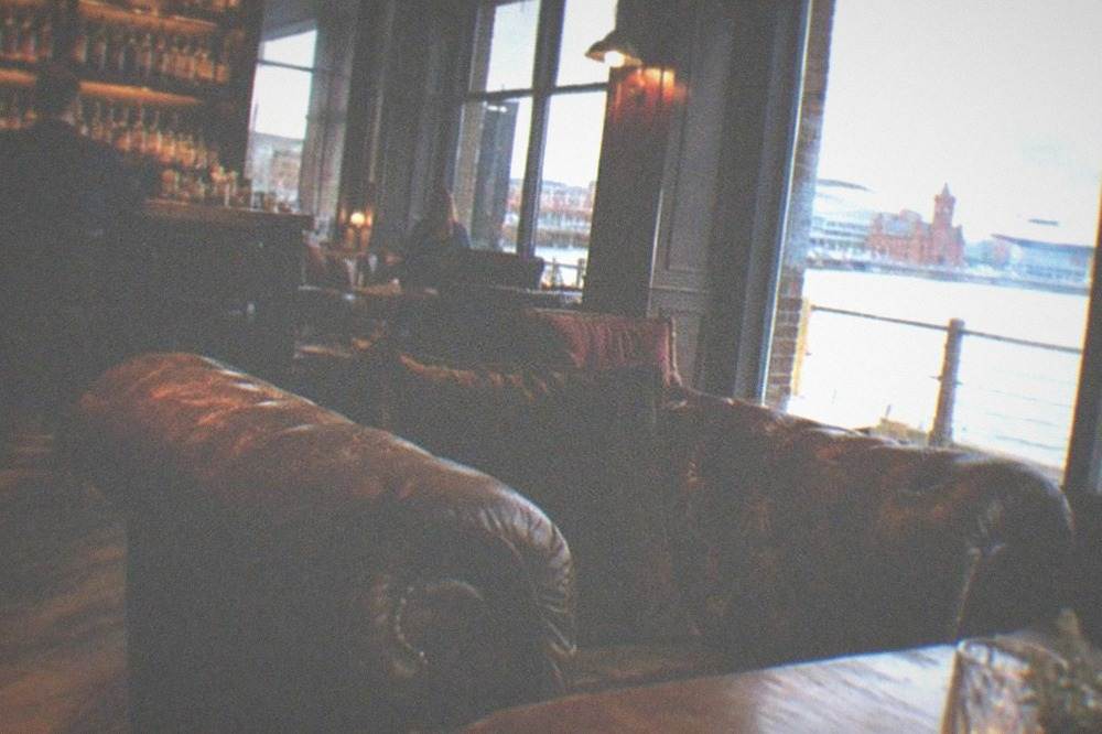 A dimly lit bar interior with leather sofas and shelves of spirit bottles