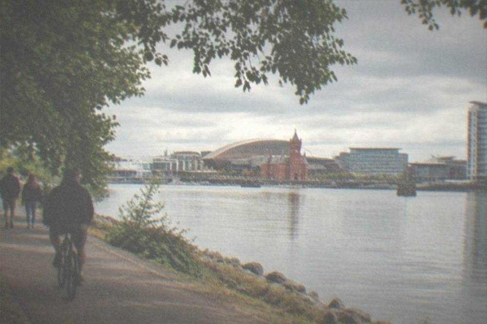Tree-lined riverside path with walkers and cyclists beside calm water