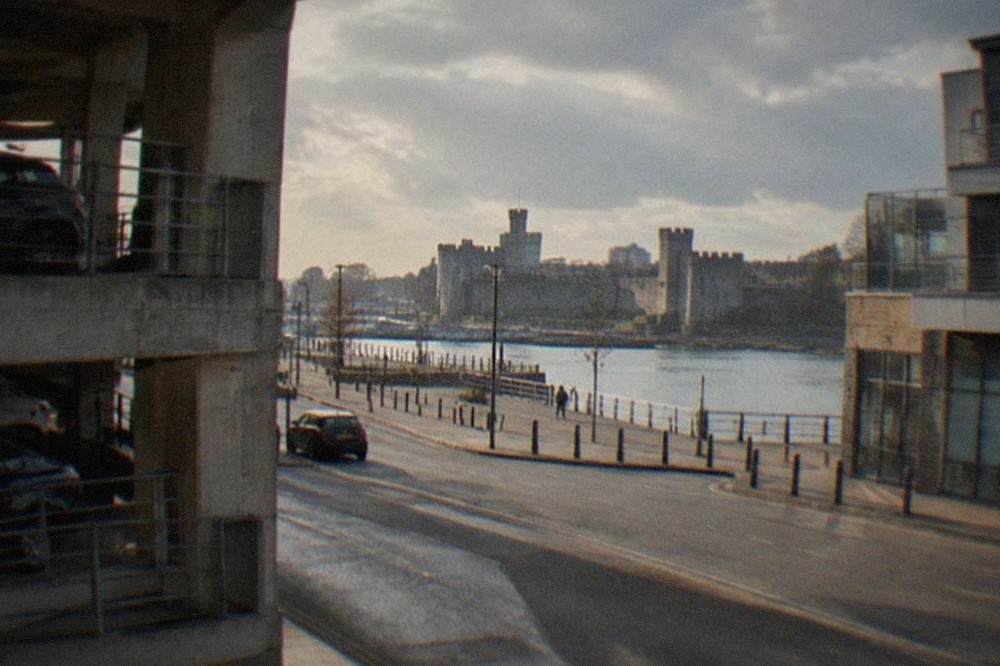 Multi-storey car park exterior beside a Cardiff city street with shops and a castle wall in the distance