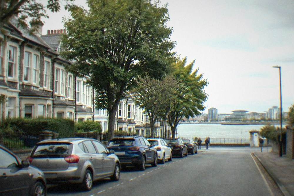 Row of parked cars along a tree-lined residential street with Victorian terraced houses