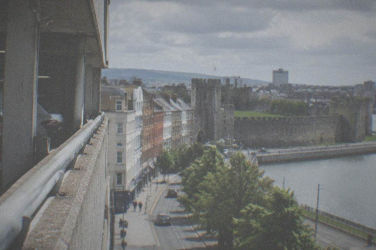 Multi-storey car park exterior beside a Cardiff city street with shops and a castle wall in the distance