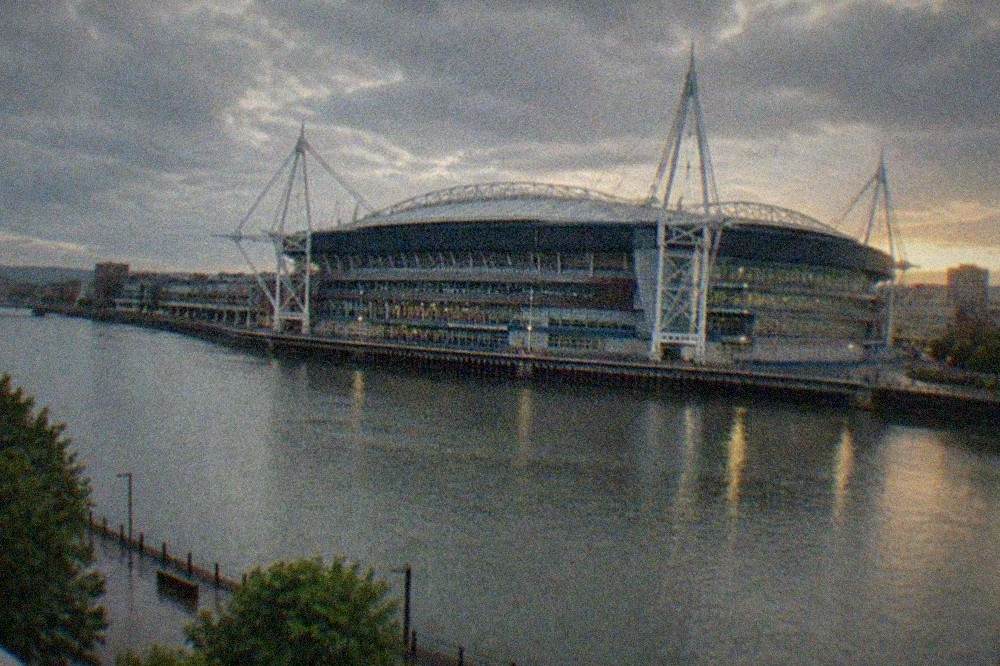A large modern stadium with a sliding roof seen from across a river at dusk