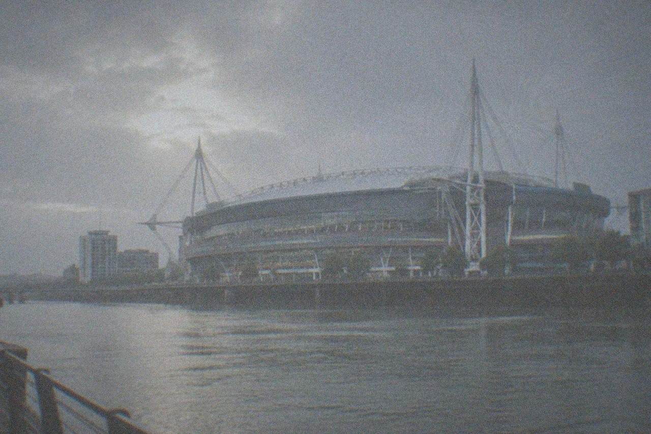 A large modern stadium with a sliding roof seen from across a river at dusk