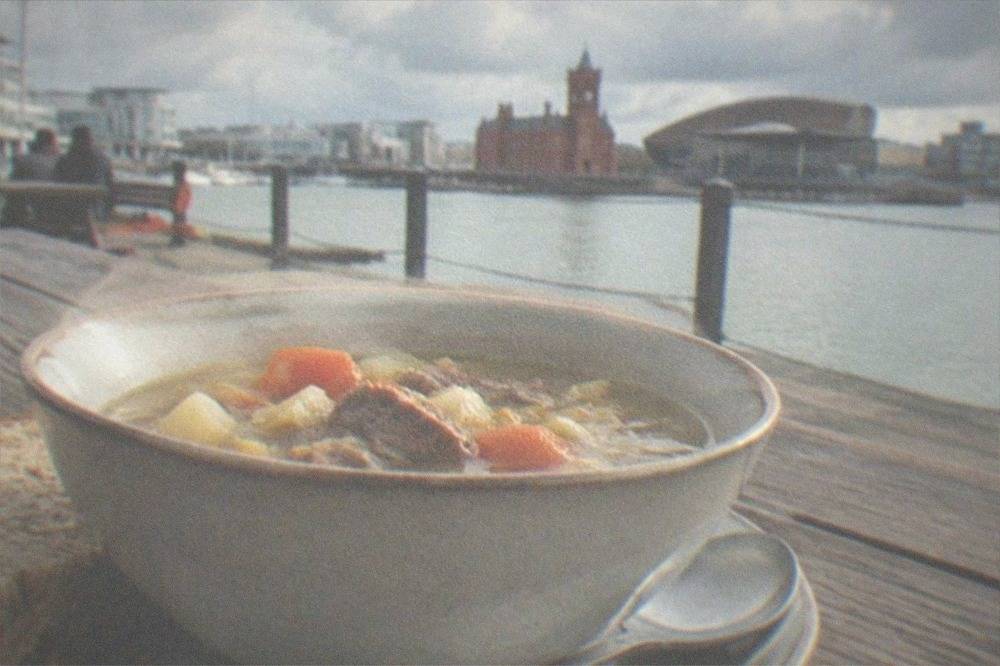 A bowl of traditional Welsh cawl soup with bread on a wooden table