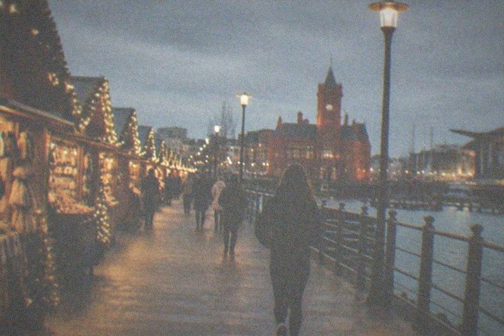 Festive wooden market stalls decorated with lights along a city street at dusk