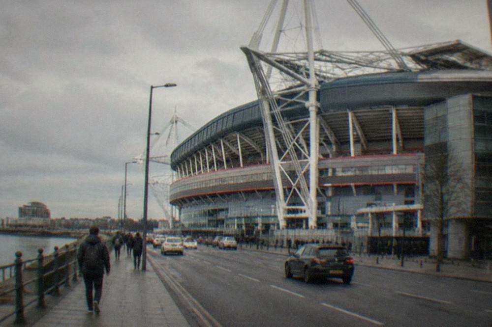 A large modern rugby stadium with a retractable roof seen from outside on a busy city street