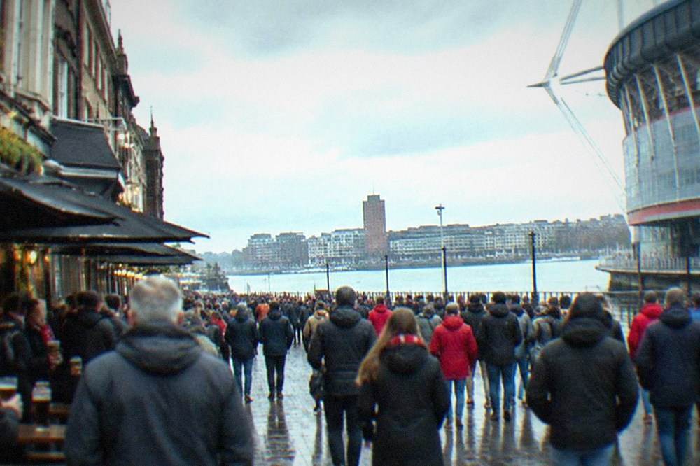 A crowded pedestrian street lined with pubs outside a stadium before a rugby match