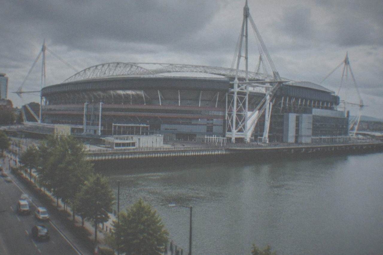 A large modern rugby stadium with a retractable roof seen from outside on a busy city street