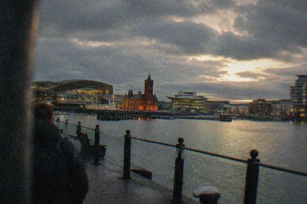 Evening view across Cardiff Bay with illuminated buildings and a waterfront walkway