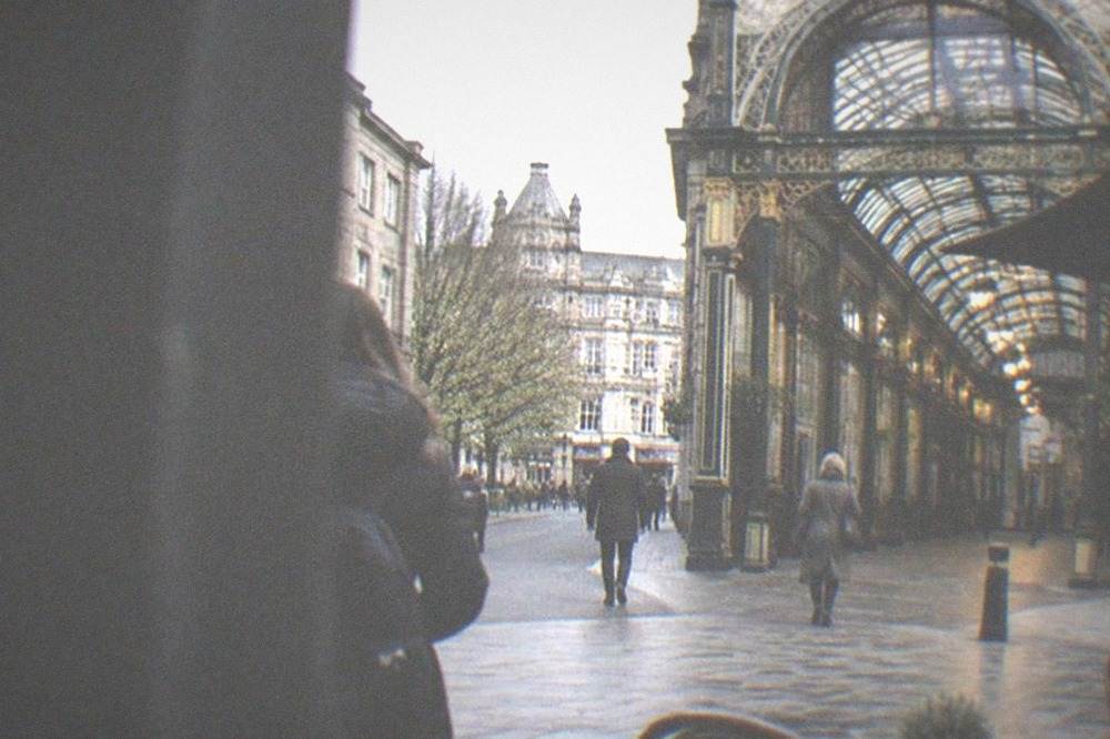 Pedestrian street in central Cardiff with ornate Victorian arcade entrance and cafe tables