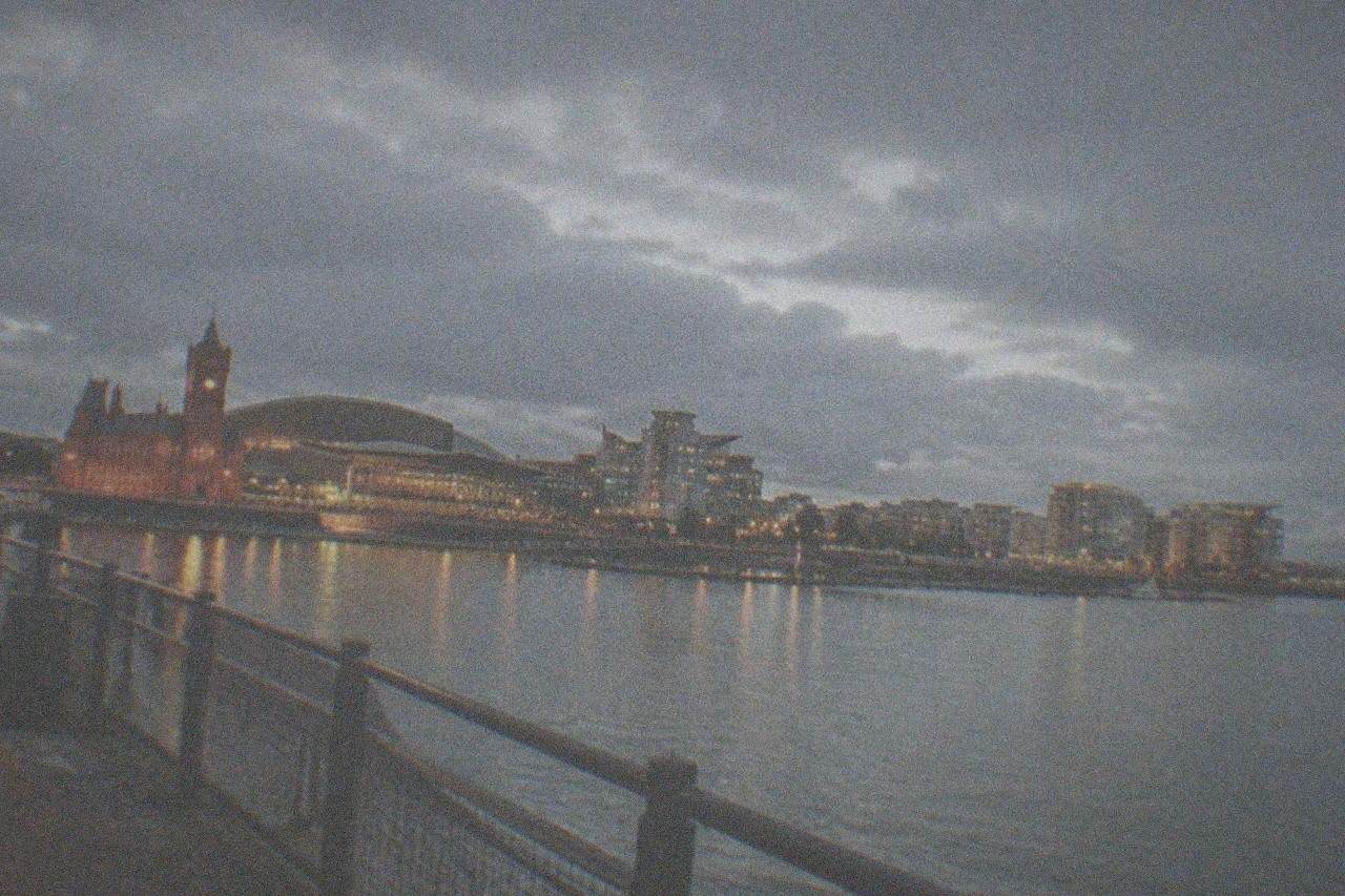 Evening view across Cardiff Bay with illuminated buildings and a waterfront walkway