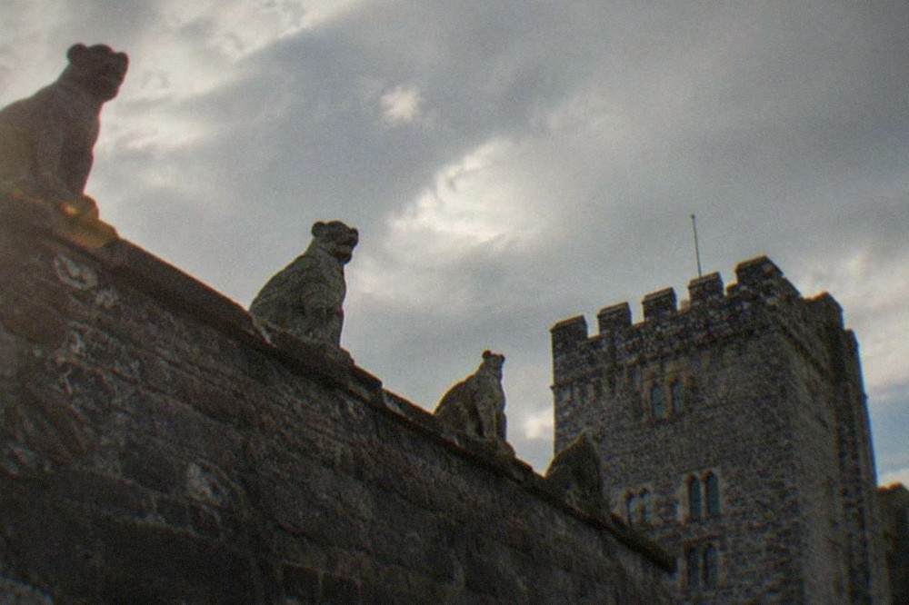 A stone wall topped with carved animal figures beside a castle tower