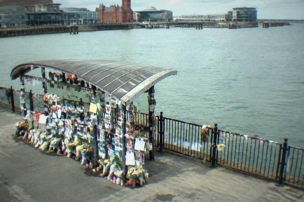 A covered memorial covered in notes and photographs beside a waterfront