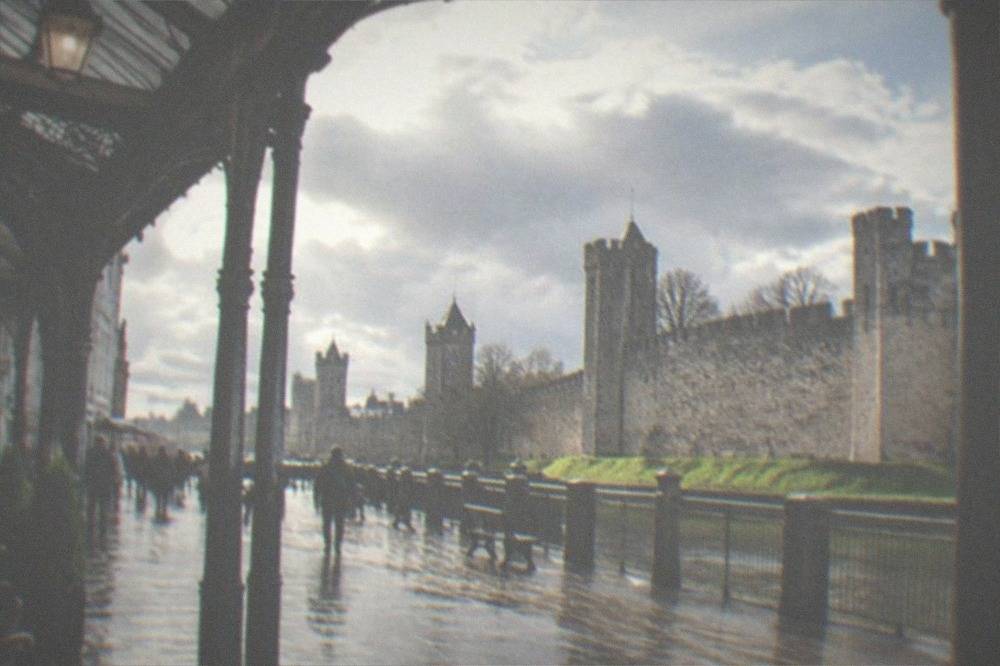A city street with Victorian arcades and a castle wall in the background
