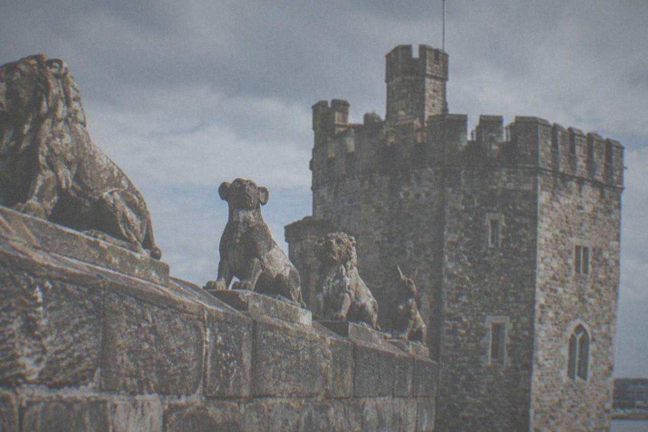 A stone wall topped with carved animal figures beside a castle tower