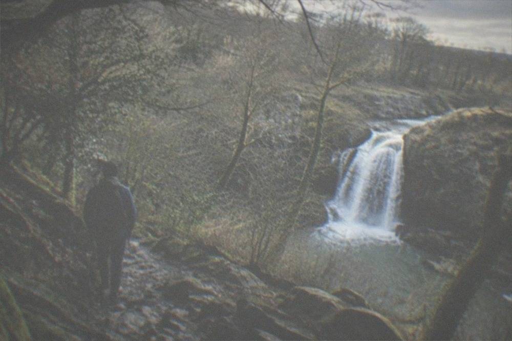 A hiker on a rocky trail descending through oak woodland towards a waterfall