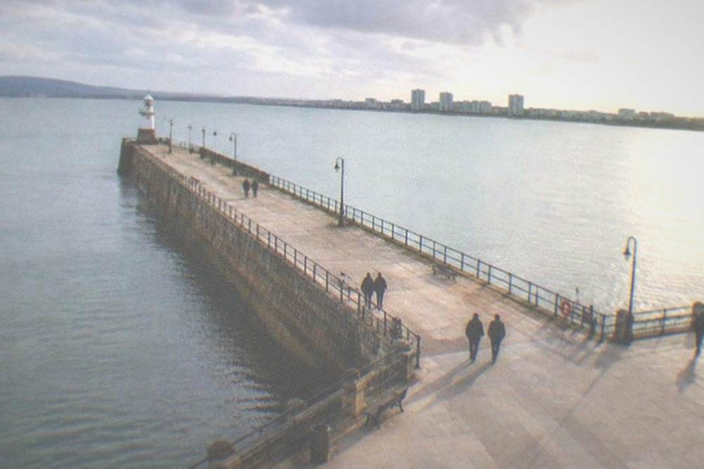 A stone pier reaching into a calm sea beside a wide esplanade