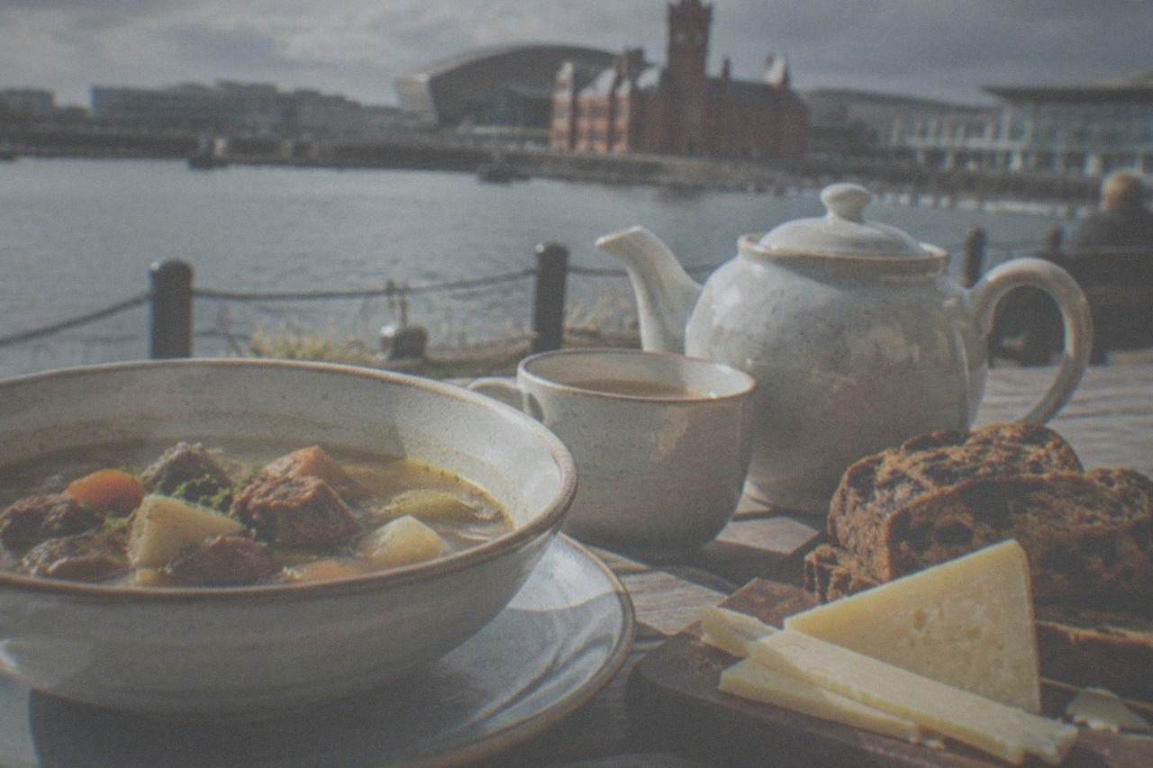 A table laid with a bowl of lamb cawl, Welsh cheese and sliced bara brith beside a teapot