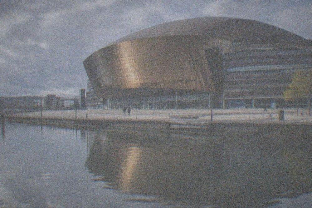 The Wales Millennium Centre facade reflected in the still water of Cardiff Bay at dusk