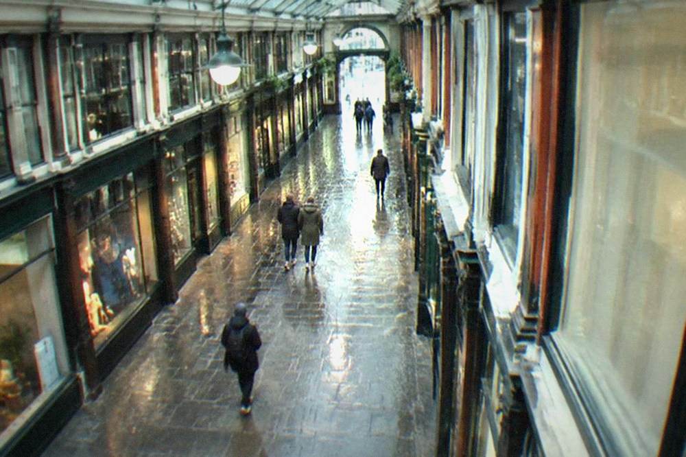 Interior of a covered Cardiff arcade with shopfronts and a glass roof on a grey day